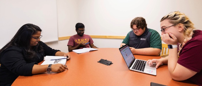 Four students are studying at a round table inside a group study room.