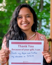 a smiling woman holding a sign that says, thank you. Because of your gift, I can finish my degree and further my education in STEM.