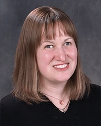 Tracy Davis portrait showing head and shoulders, smiling, on a gray background