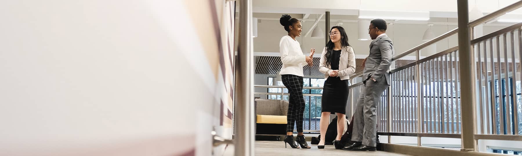 Three students in business clothing talking near a railing.