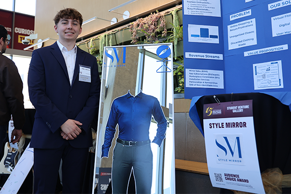 Photo of a student standing in front of his venture display board at the New Venture Challenge