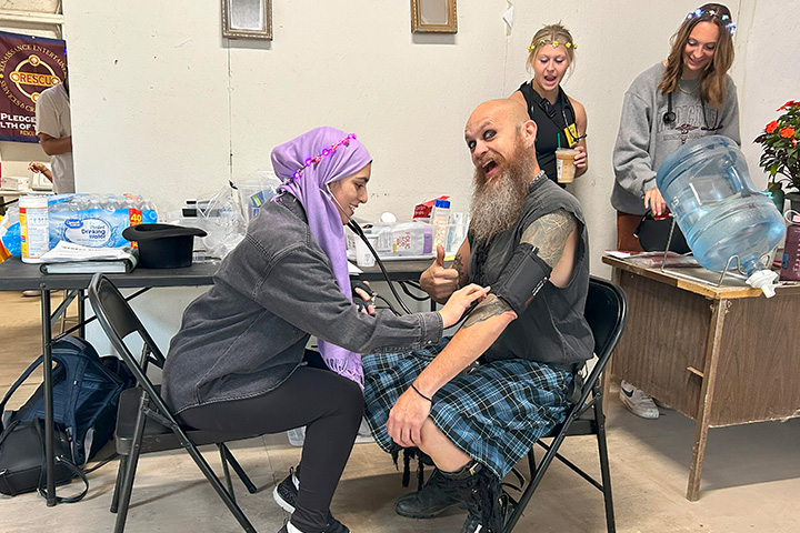 A man in a kilt with a thick beard gets his blood pressure checked at a rustic health clinic.