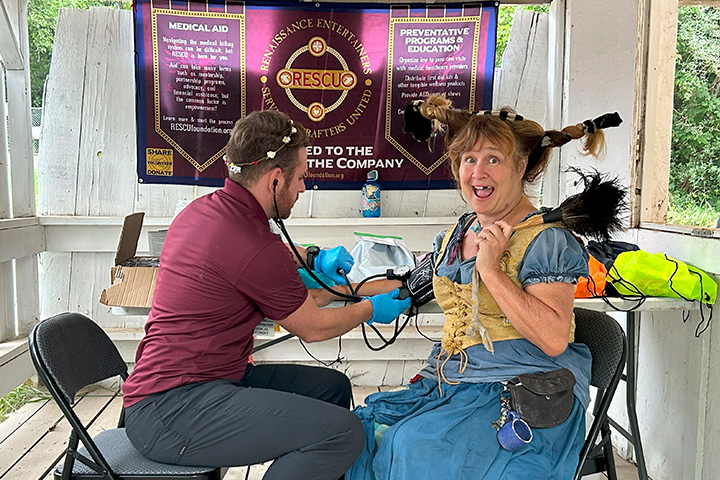 A woman in renaissance attire gets her blood pressure checked at a rustic health clinic.