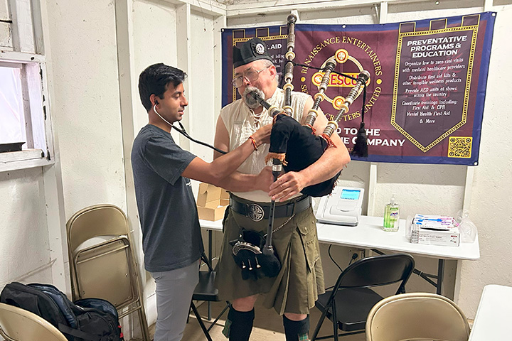 A Scottish man in a kilt plays the bagpipes while he gets his heart checked at a rustic health clinic.