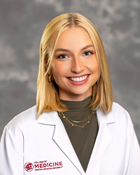 A female medical student in a white lab coat embroidered with a Central Michigan University College of Medicine logo.