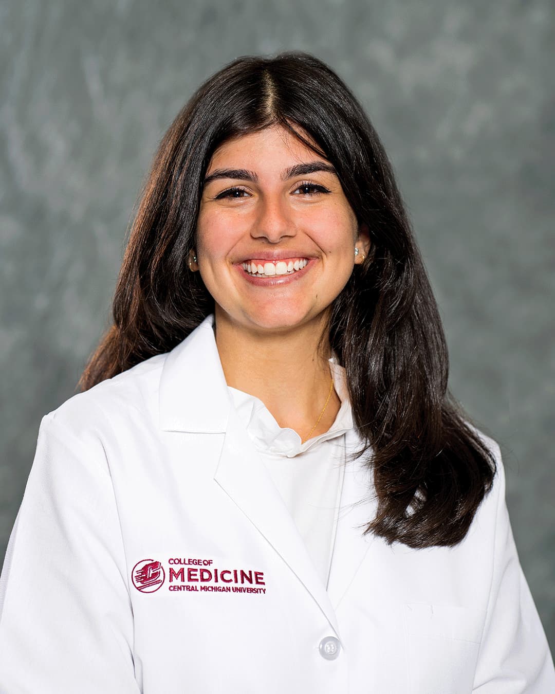 A female CMU College of Medicine medical student wearing her white coat as she smiles for the camera.