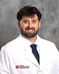 A male CMU College of Medicine medical student wearing his white coat as he smiles for the camera.