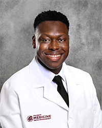 A male CMU College of Medicine medical student wearing his white coat as he smiles for the camera.