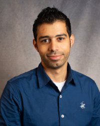 A man with short dark hair wearing a blue collared shirt.