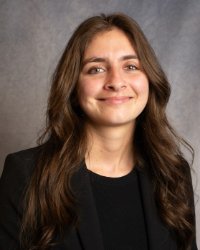 A women with long brown hair in a dark suit smiling.