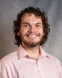 A man with curly hair and beard wearing a pink button down shirt.