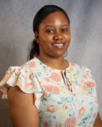 A woman in a floral shirt smiles for a professional headshot in front of a grey background.