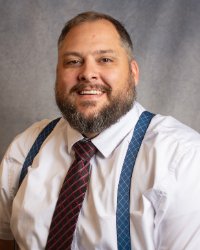 A man wearing blue suspenders, a maroon tie and a white shirt.