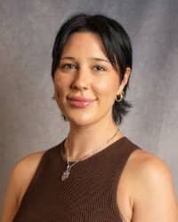 A woman with short dark hair wearing a brown tank top.