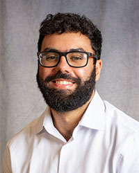 Nader Hanna has a dark beard and is wearing a white shirt and glasses.