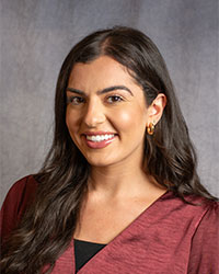 Selena Kassab has long dark hair and is wearing a burgundy and black blouse.