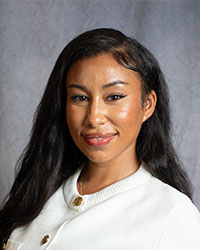 Nabta Laz is wearing a white cardigan and has long, dark hair.