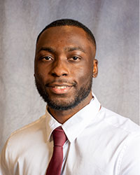 Olusayo Oketokun is wearing a white button down shirt and a red tie.