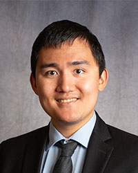 Kevin Qin is wearing a black blazer, grey shirt, and black tie.