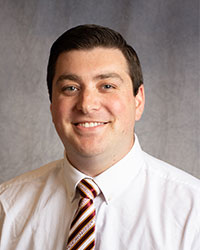 Nicholas Rincon is wearing a white button down shirt with a red and white striped tie.