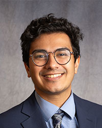 Aditya Shah is wearing a blue blazer, light blue shirt, and grey tie.