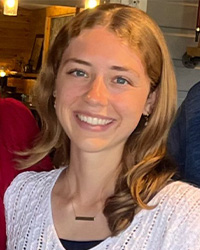 A woman with long blond hair wearing a black shirt and white sweater smiles at the camera.