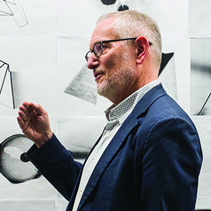 Artist Martin Venezky speaking while standing in front of one of his pieces of art