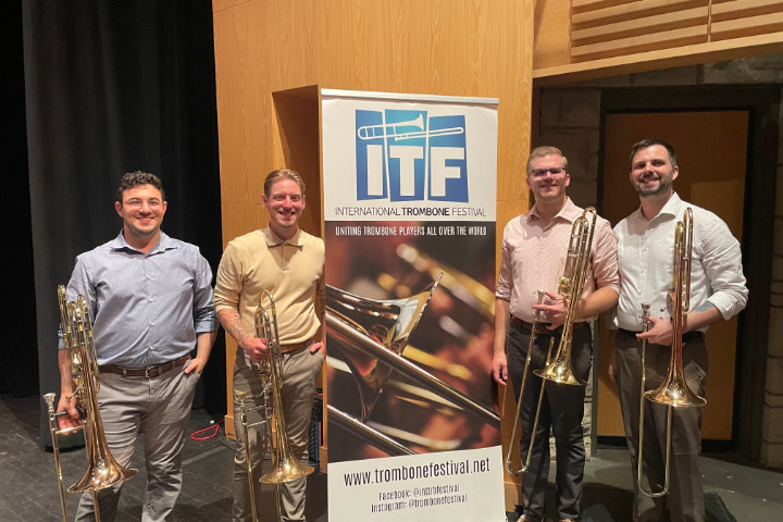 a group of men holding trombones while standing in front of a banner titled International Trombone Festival