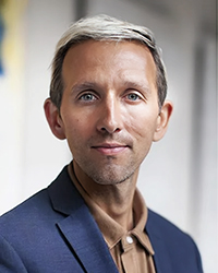 Headshot of Andrew Dost. He's wearing a tan shirt with a blue jacket.