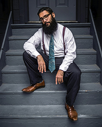 Photo of Jake May dressed in a tie and suspenders, sitting on the stairs.