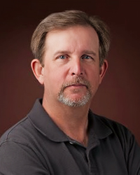 Headshot of Jay Beckman on a brown backdrop.
