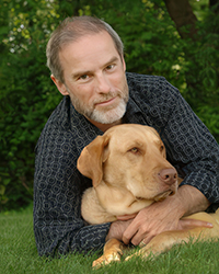 John Grogan and his golden lab Marley posing under a tree on the grass.
