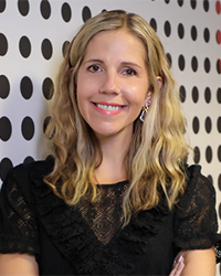 Headshot of Nikki Little. She is leaning against a white wall with black polka dots.
