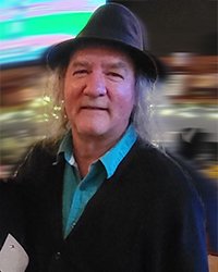 Headshot of Roger Hitts. He's holding a cube with a 25 on it. There's a computer in the background.