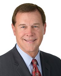 Headshot of Dave LewAllen wearing a dark suit coat, light blue dress shirt and dark red tie against a bright white backdrop