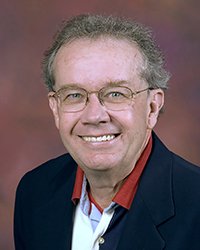 Headshot of Joe Misiewicz wearing a dark blue blazer and red collared shirt against a soft maroon backdrop.