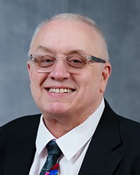 Headshot of Tom Caylor set in front of a blue backdrop.