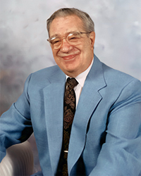 Headshot of Gilbert R Maienknecht in a blue suit in front of a soft blue backdrop.