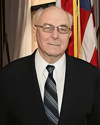 Headshot of Fred Mester in a suit and tie in front of an American flag