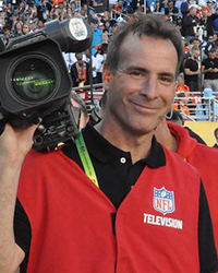 Headshot of Don Cornelli. He's on the field, wearing his official NFL Television vest, holding a video camera.