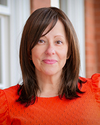 Headshot of Lisa Yanick Litwiller in front of a brick building with white frames windows.
