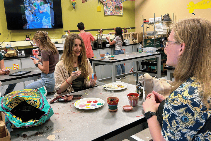 Two college students paint terra cotta pots while smiling.