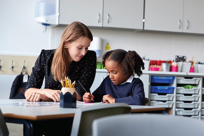 A school counselor sitting with a young child in a classroom.