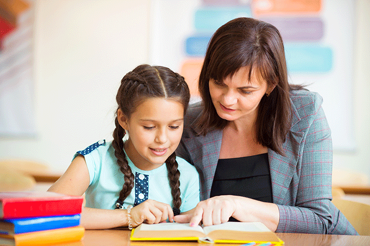 Adult assisting a child with long braided hair read a book