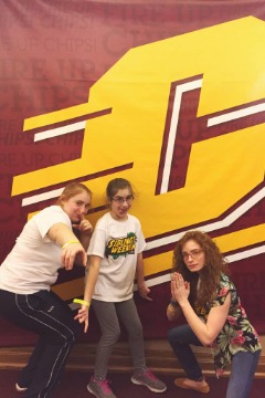 Alexis Gostlin, Chloe Straub, and Sarah Spearing posting in front of a big banner with the Action C on it.