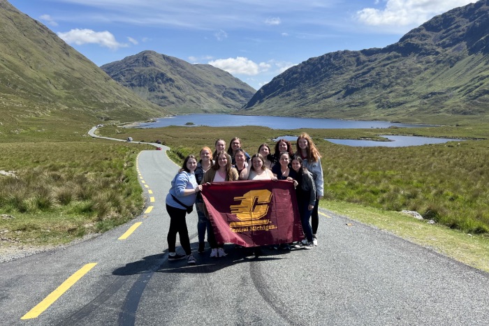 Students posing in front of mountains in Ireland with the CMU flag.