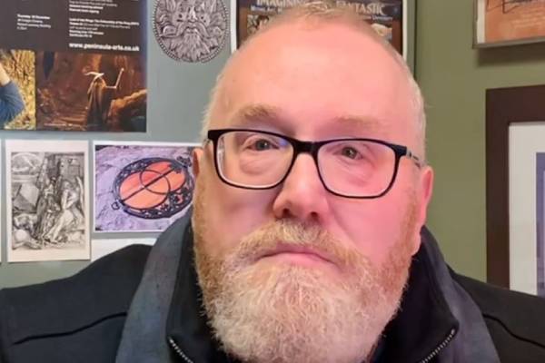 Ari Berk, an English professor with dark-framed glasses and a dark coat, faces the camera.