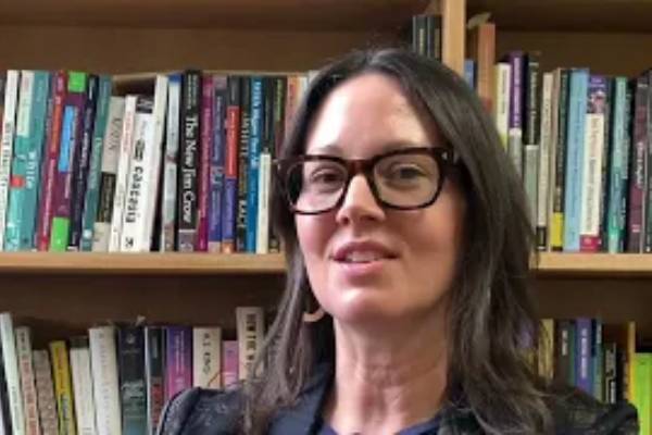 Carlin Borsheim-Black looks at the camera in front of a set of full bookshelves.