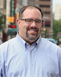Closeup image of Jim Ananich wearing a light blue button up shirt and glasses