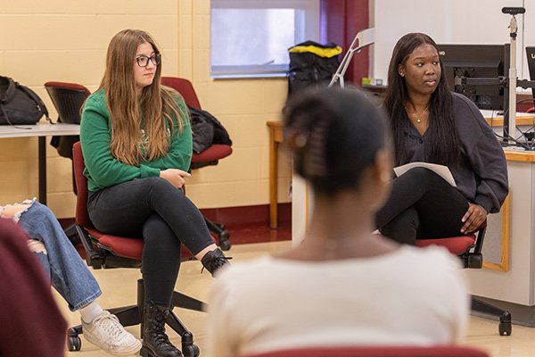 A group of students sitting in maroon chairs in an Anspach Hall classroom